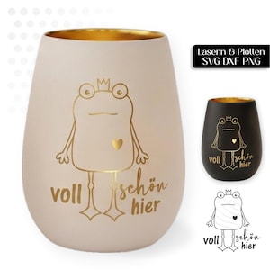 May include: A matte beige tumbler with a gold interior featuring a gold line drawing of a frog wearing a crown with a small heart on its chest and the German text "voll schön hier" printed in gold script below the frog figure.