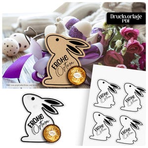 May include: Easter decorations with bunny-shaped cutouts, the text "Frohe Ostern", and a chocolate candy. The image shows a basket with decorated eggs, purple ribbon, and flowers. Additional bunny cutouts are also visible.