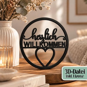 Könnte beinhalten: Ein schwarzes, kreisförmiges Schild mit dem deutschen Schriftzug "herzlich WILLKOMMEN" in einer Kombination aus Schreib- und Blockschrift sowie einem herzförmigen Ausschnitt am unteren Rand. Ein kleines Etikett zeigt den Text "3D-Datei inkl. Lizenz".