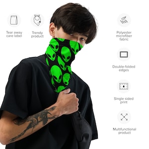 Könnte beinhalten: Eine schwarze und grüne Gesichtsmaske mit einem sich wiederholenden Muster aus grünen Alienköpfen. Die Maske besteht aus Polyester-Mikrofasergewebe und hat doppelt gefaltete Kanten. Es handelt sich um einen einseitigen Druck und kann für mehrere Zwecke verwendet werden.