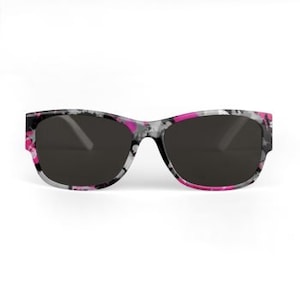 May include: Sunglasses with a black frame and dark lenses. The frames have a pattern of pink, white, and black floral designs. The sunglasses are set against a white background.
