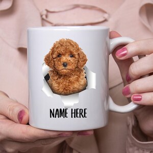 May include: White ceramic mug with a brown and white poodle peeking out of a torn hole in the mug. The text "NAME HERE" is printed on the mug.