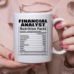 May include: White ceramic coffee mug with a black and white graphic of a nutrition facts label for a "Financial Analyst". The label lists various skills and attributes with a percentage daily value for each. The text at the bottom of the label reads "* Not A Significant Source Of Gratitude Received. ** Percent Daily Values Are Based On Your Unique Diet."