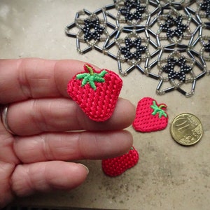 Könnte beinhalten: Drei rote gestickte Erdbeer-Patches mit grünen Blättern. Die Patches befinden sich auf einer Hand und einem Tisch.