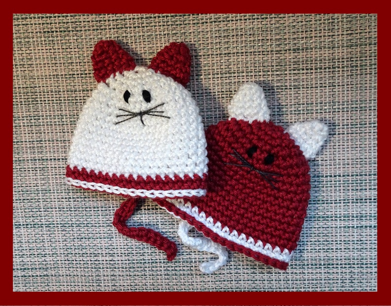 May include: Two crocheted cat hats, one white with a red trim and one red with a white trim. Both hats have black embroidered eyes and whiskers.