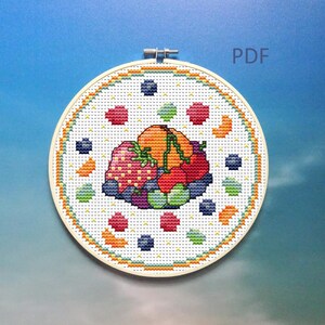 Könnte beinhalten: Eine Kreuzstich-Stickerei mit einem farbenfrohen Obstkorb-Design. Das Design umfasst Erdbeeren, Blaubeeren, Orangen und einen Kürbis, alles in einem kreisförmigen Rahmen. Der Text "PDF" ist oben rechts sichtbar.
