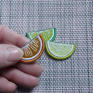 Könnte beinhalten: Drei gestickte Bügelbilder von Fruchtscheiben. Eine Orangenscheibe und zwei Limettenscheiben. Die Limettenscheiben sind grün und gelb, und die Orangenscheibe ist orange und gelb.