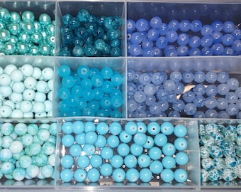 May include: A divided container filled with various shades of blue and turquoise beads. The beads are round and come in different finishes, including glossy, crackled, and speckled. Ideal for jewelry making and crafting.