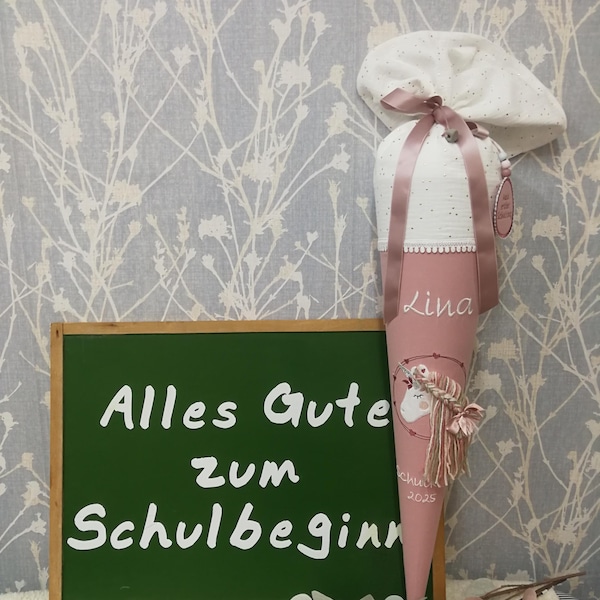 Può includere: Un cono scolastico rosa e bianco con un design a unicorno, un cappello abbinato e una lavagna con la scritta "Alles Gute zum Schulbeginn". Il cono è legato con un nastro rosa.