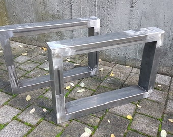 May include: Two metal table legs made of square steel tubing. The legs are welded together to form a rectangular frame. The legs are unfinished and have a raw metal finish.
