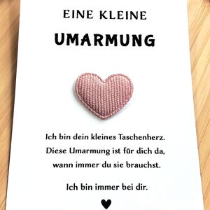 Könnte beinhalten: Eine weiße Karte mit deutschem Text, darunter "EINE KLEINE UMARMUNG". Ein kleines, rosa Herz ist auf der Karte zentriert. Die Botschaft der Karte ist ein tröstliches Gefühl.