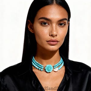 Peut inclure: Collier à plusieurs rangs de perles turquoises avec un pendentif en forme de rose turquoise et un accent de perle blanche. Le collier est porté par une personne portant une chemise noire. Le collier est de style ras du cou.