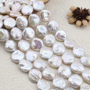 May include: Strands of lustrous, white, coin-shaped pearls. The pearls have a natural, iridescent sheen, reflecting light. The image also includes a dried flower and the text "YouPearlSandDIY".