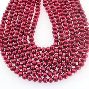 以下が含まれることがあります： 濃い赤色の淡水真珠のネックレス。真珠は丸くて滑らかで、緩やかな流れのあるパターンで配置されています。