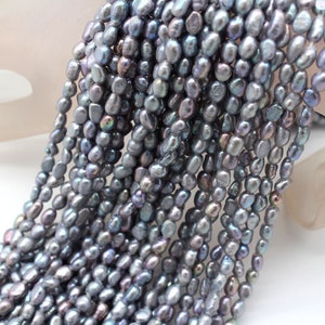 May include: A strand of gray freshwater pearls with an iridescent sheen. The pearls are irregularly shaped and have a slightly elongated oval form.