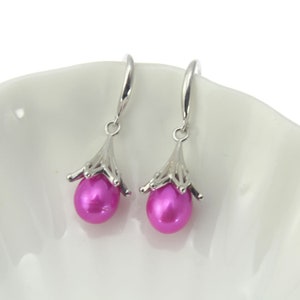 May include: A pair of silver dangle earrings with pink pearl drops. The earrings feature a delicate, intricate design.