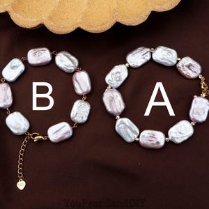 Puede incluir: Dos pulseras de perlas, etiquetadas A y B, se muestran sobre una superficie marrón. Cada pulsera presenta perlas grandes, de forma irregular, de color lila claro y blanco, ensartadas con cierres y cadenas doradas. Vista superior.