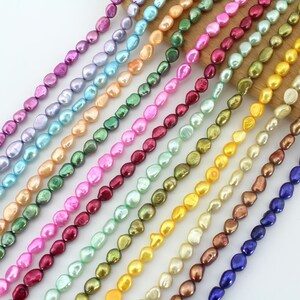 May include: A strand of iridescent baroque pearls in various colors, including blue, green, pink, and gold. The pearls are strung on a clear thread and are arranged in a line.