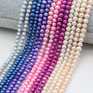 May include: A strand of pearls in various colors, including white, pink, purple, blue, and gray. The pearls are strung together on a thin thread and are arranged in a rainbow pattern.