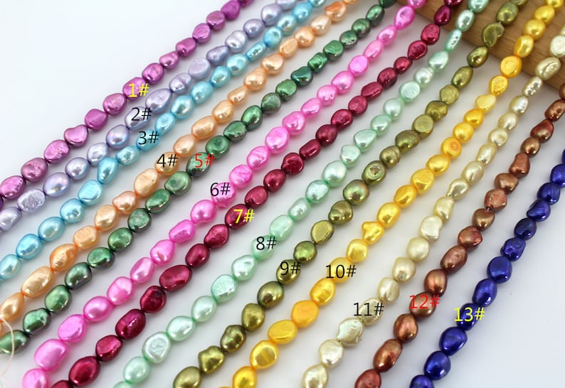 May include: A strand of 13 different colors of baroque freshwater pearls. The pearls are all different shapes and sizes, and they are strung on a white thread. The pearls are labeled with numbers 1 through 13.