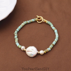 May include: A bracelet featuring small, light blue-green disc-shaped beads, two small white pearls, and one large, irregular white baroque pearl in the center. The piece is secured with a gold-toned metal toggle clasp. The text YouPearlSandDIY is visible.