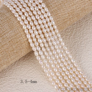 May include: A strand of white freshwater pearls, approximately 3.5-4 mm in size, displayed on a beige burlap fabric background. The pearls are oval shaped and have a smooth, lustrous finish.