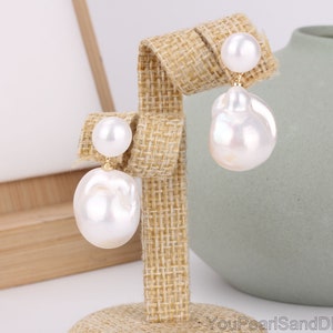 May include: A pair of white baroque pearl drop earrings with gold posts. The pearls are irregular in shape and have a high luster.