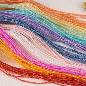 Könnte beinhalten: Eine Sammlung bunter Edelsteinperlen, die in Reihen angeordnet sind und eine Vielzahl von Farbtönen und Texturen zeigen. Die Perlen sind klein und gleichmäßig in der Größe, perfekt für die Schmuckherstellung.