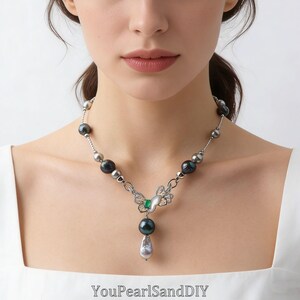 Può includere: Una collana d'argento con un ciondolo a farfalla, una gemma verde e una grande perla a goccia. La collana include anche perle grigio scuro e argento. Il testo "YouPearlSandDIY" è visibile in basso.