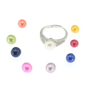 May include: A silver adjustable ring with a large white pearl center stone, surrounded by smaller clear stones. Scattered around the ring are several colorful pearls in shades of pink, orange, green, yellow, blue, and red.
