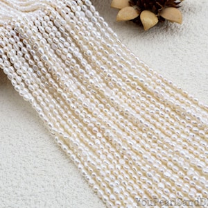 May include: Strands of creamy white, oval-shaped freshwater pearls. The pearls are strung together, creating a flowing, textured appearance. The pearls are a natural off-white color, and the image is well-lit, highlighting the luster of the pearls.