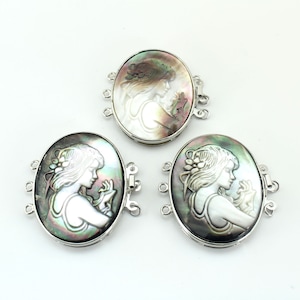 Puede incluir: Tres cierres ovalados de plata con un diseño tallado de un perfil de mujer en nácar. Los cierres tienen cuatro bucles para sujetar a un collar o pulsera.