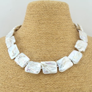 May include: A white pearl necklace with square-shaped pearls. The necklace is on a brown mannequin.