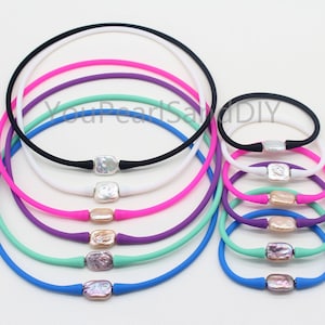 May include: A set of colorful silicone necklaces with a pearl charm. The necklaces are available in black, white, pink, purple, green, and blue. The pearls are a variety of colors, including white, pink, and purple.