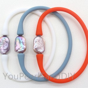 May include: Three colorful bracelets. Each bracelet features a large, iridescent, baroque pearl bead. The bracelets have white, blue-gray, and orange silicone bands. The pearls have a mix of pink, purple, and silver tones.