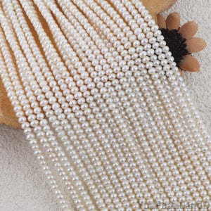 May include: Close-up of multiple strands of small, white pearls. The pearls are uniform in size and shape, creating a smooth, lustrous surface. The strands are arranged closely together, suggesting a jewelry-making supply or finished product.