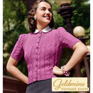 Puede incluir: Un cárdigan magenta de estilo vintage con mangas cortas y diseño de punto trenzado. El suéter tiene cuello blanco y pequeños botones en la parte delantera. El logotipo de Goldmine Vintage Knits está en la esquina inferior derecha.