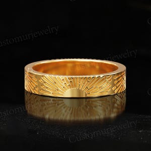 May include: A gold band ring with a sunburst design. The ring is smooth and shiny.
