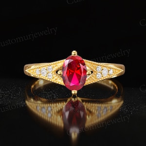 May include: A gold ring with a large oval ruby center stone and small diamond accents. The ring has a detailed design on the band and is set against a black background. The text "Customurjewelry" is visible.