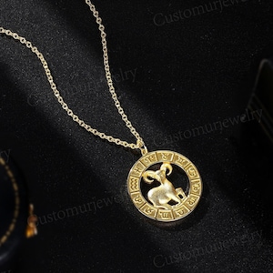 May include: Gold necklace with a zodiac pendant featuring a ram inside a circle with Roman numerals and astrological symbols.
