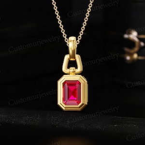 May include: A gold-colored necklace with a rectangular, ruby-red pendant. The pendant is framed in gold and hangs from a delicate chain. The words "Customurjewelry" are visible on the image.