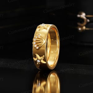 A gold ring with a shell and starfish design is displayed against a black background.