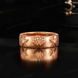 A gold ring with a seashell design and small diamonds, placed on a black surface.