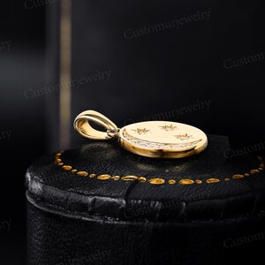A gold-colored pendant with a crescent moon design and three stars is displayed on a black leather surface.