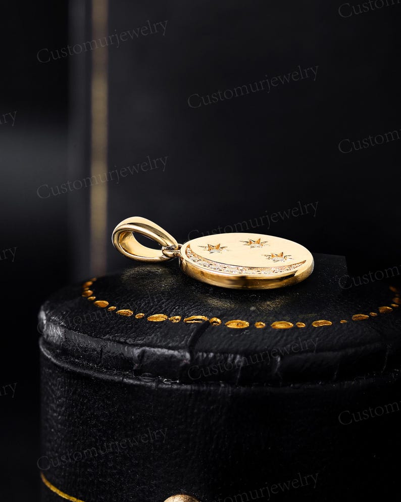 A gold-colored pendant with a crescent moon design and three stars is displayed on a black leather surface.