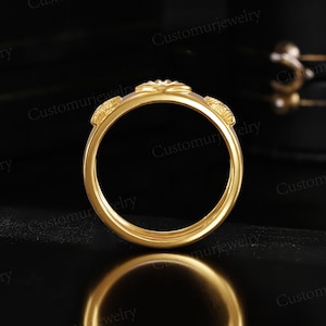 A gold ring with a floral design is displayed against a black background, reflecting on a surface.