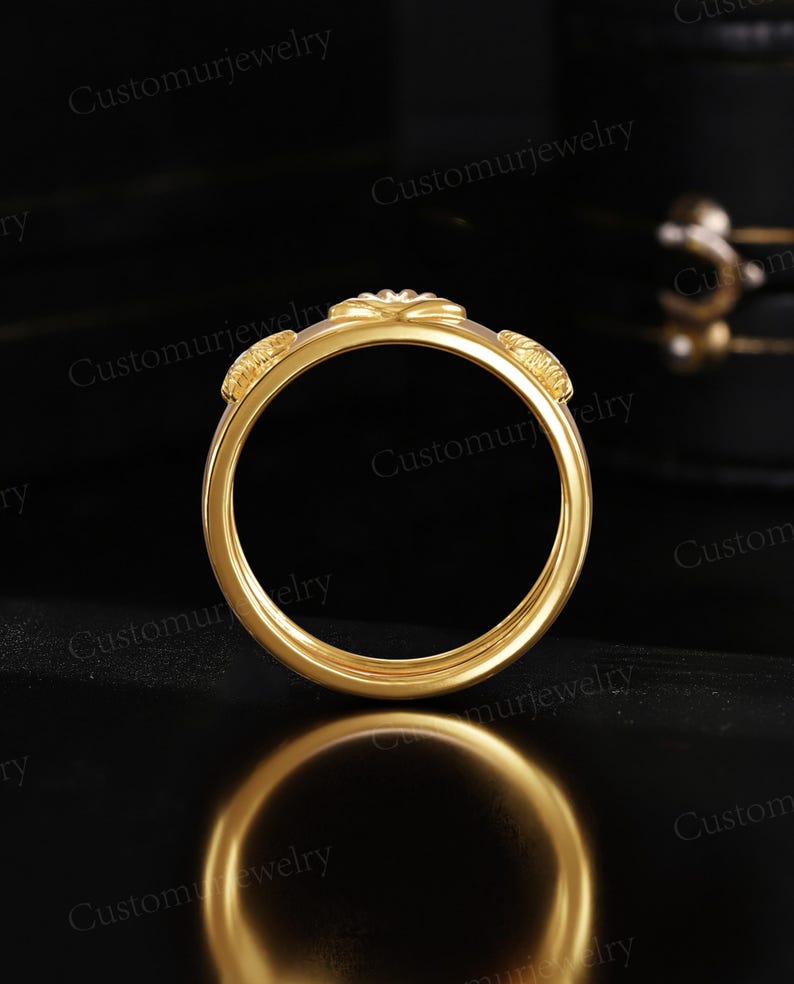 A gold ring with a floral design is displayed against a black background, reflecting on a surface.