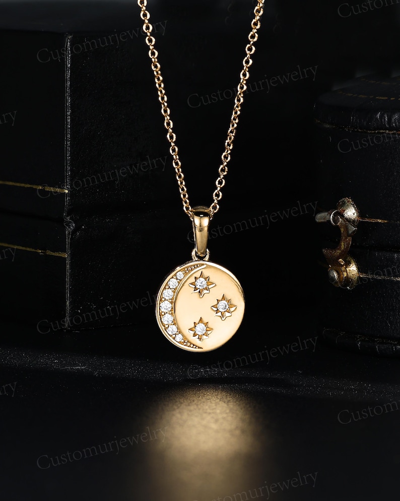 A gold necklace with a circular pendant featuring a crescent moon design and three small stars.