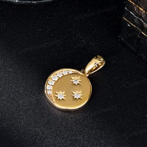A gold pendant with a crescent moon and three stars is displayed on a black surface.