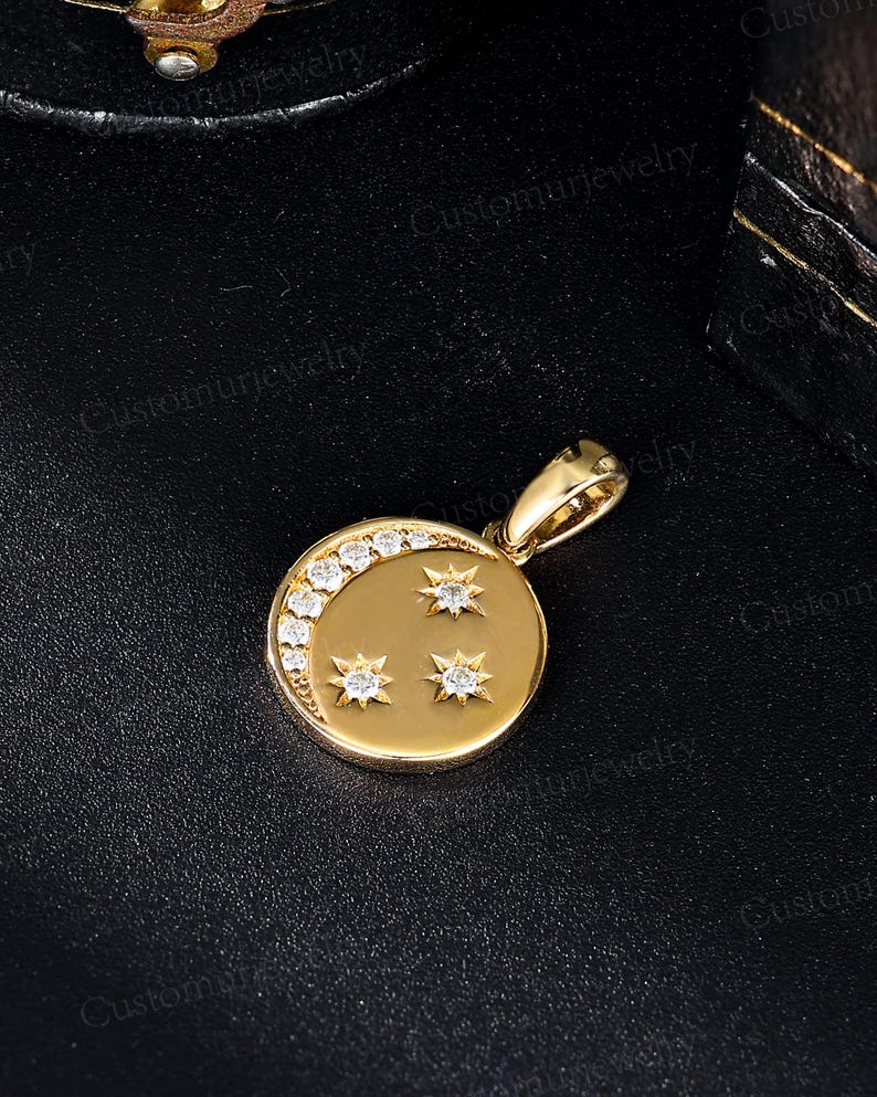 A gold pendant with a crescent moon and three stars is displayed on a black surface.